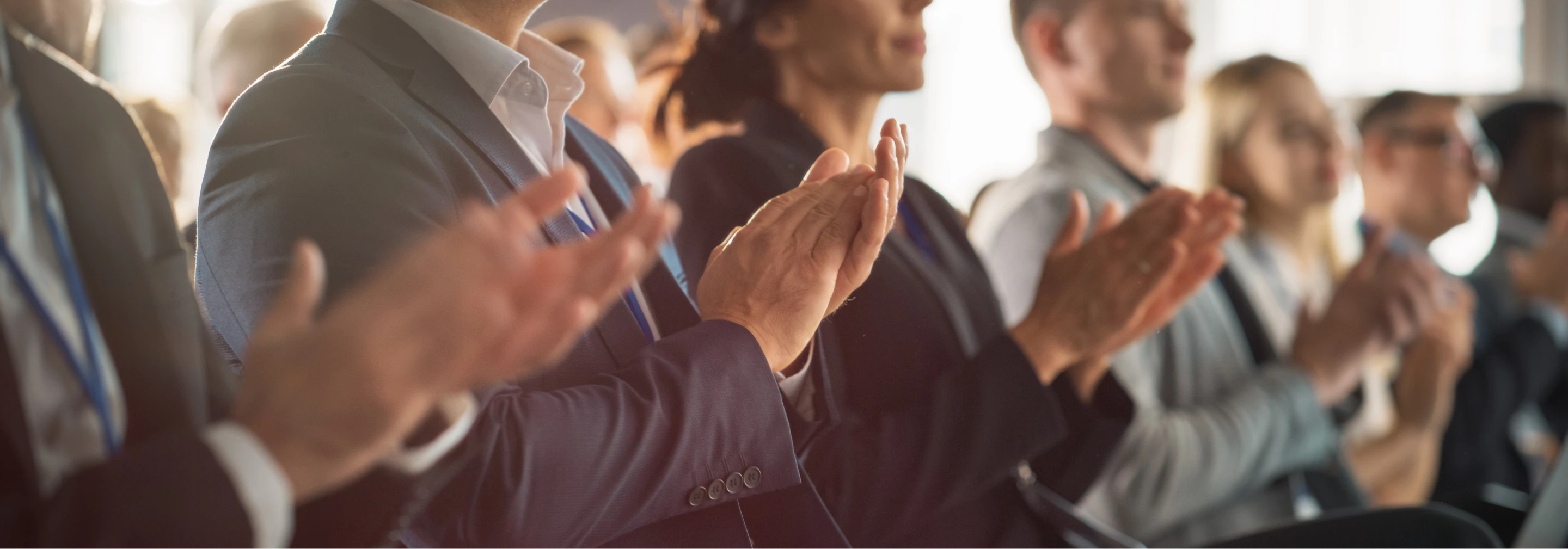 Audience members in business attire clapping their hands at a conference or presentation
