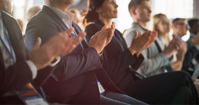 Audience members in business attire clapping their hands at a conference or presentation